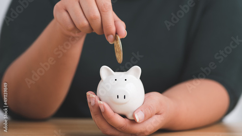 Close-up woman's hand holding a gold coin in a white piggy bank. Save money and financial investment.