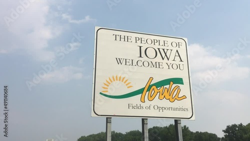 Welcome to Iowa sign pan from left to right under blue sky and bright afternoon sunlight.