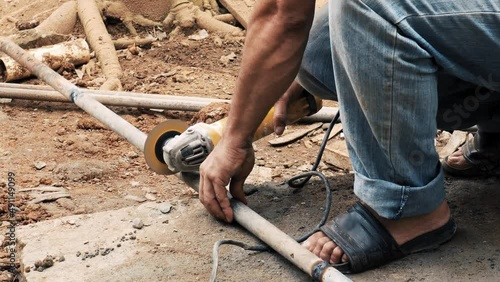 Man cutting a galvanized steel tube with an industrial electric angle grinder to elaborate a metal structure in a rural environment construction site worplace photo