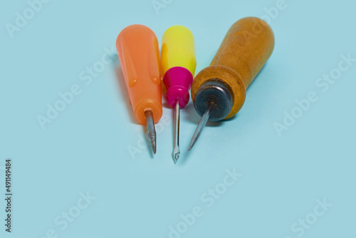 Sewing. Three multicolored awls on a blue background. 