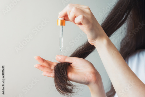 Obraz na płótnie A woman with dark hair applies a cosmetic product to the ends of her hair with a pipette