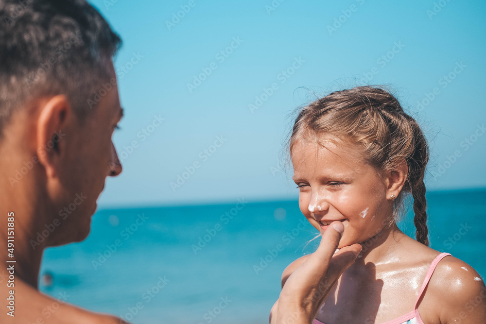 Father applying protective cream to her daughter's face at the beach. Man hand holding sunscreen lotion on baby face. Cute little girl with a sun block by the sea . Copy space. Father applying protective cream to her daughter's face at the beach. Man hand holding sunscreen lotion on baby face. Cute little girl with a sun block by the sea . Copy space.
