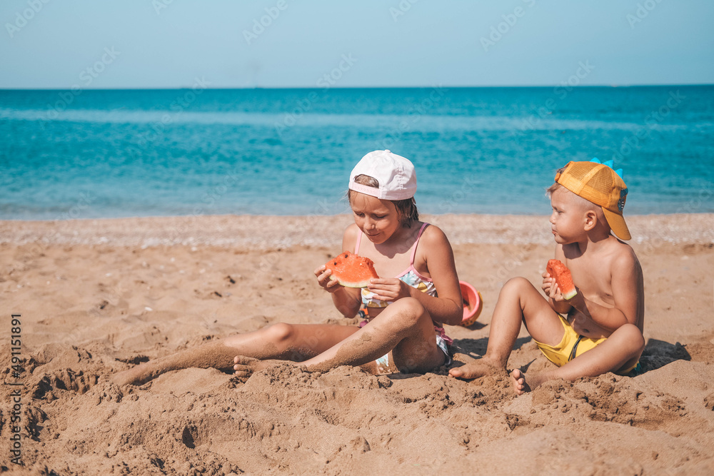 Portrait of children of sister and brother on the beach with watermelon. Girl and little boy are eating on the beach. The children had a picnic by the sea. Copy space. Portrait of children of sister and brother on the beach with watermelon. Girl and little boy are eating on the beach. The children had a picnic by the sea. Copy space.