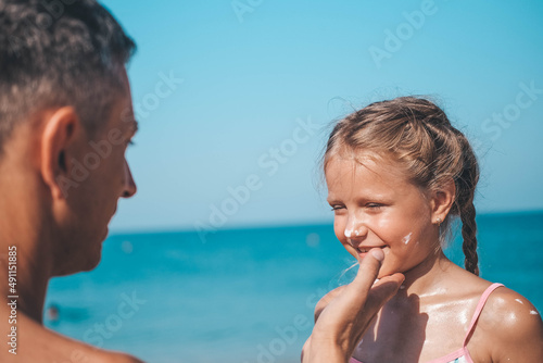 Father applying protective cream to her daughter's face at the beach. Man hand holding sunscreen lotion on baby face. Cute little girl with a sun block by the sea . Copy space. © smile35