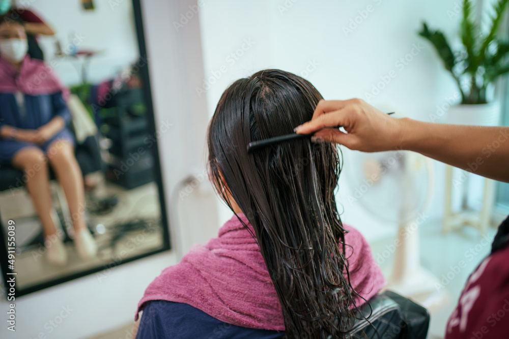Fototapeta premium Asian young woman have a hair cutting and spa by professional beauty hair dresser. Woman sitting on the chair in beauty - Salon shop while barber cutting her hair.