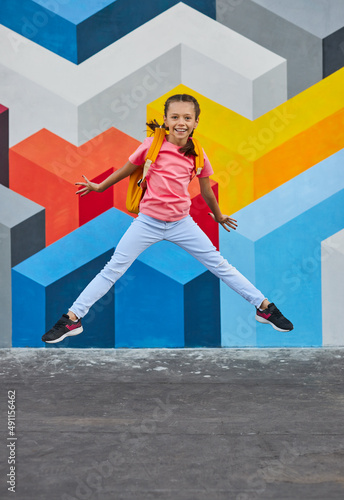 Merry schoolgirl jumping near graffiti wall