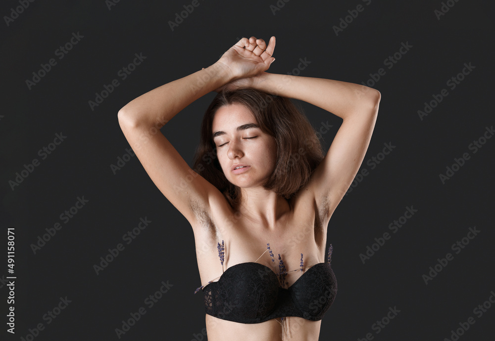 Unshaven armpit concept. Girl is holding lavender flowers in front her armpits. Symbol of unshaven body parts. Body positivity and naturalness. Problems home depilation on black background