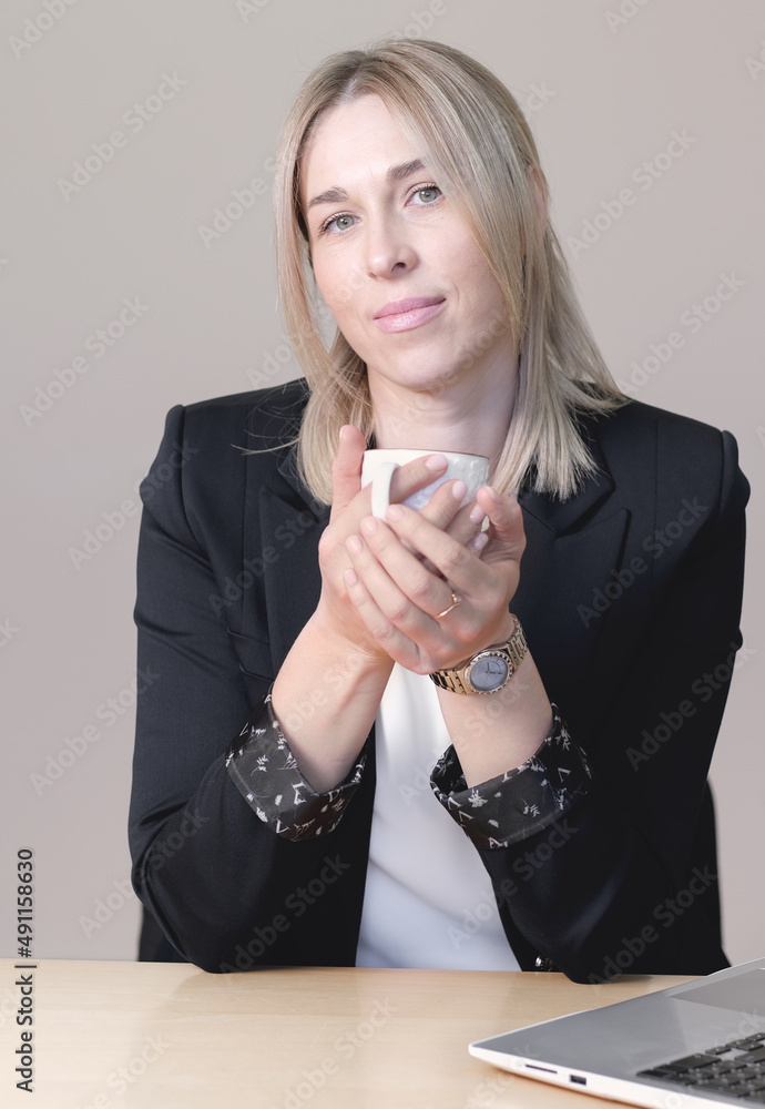 woman attorney or financial consultant or lawer wearing formal suit holding a cup of coffee looking at camera. confident sucsessful woman sitting by the desk with laptop. vertical woman attorney or financial consultant or lawer wearing formal suit holding a cup of coffee looking at camera. confident sucsessful woman sitting by the desk with laptop. vertical