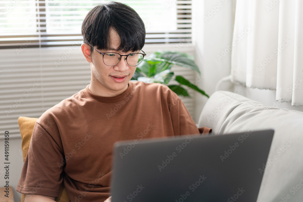 Technology Concept The man that is putting on glasses leaning his back on the dark yellow while focusing on the laptop’s screen. Technology Concept The man that is putting on glasses leaning his back on the dark yellow while focusing on the laptop’s screen.