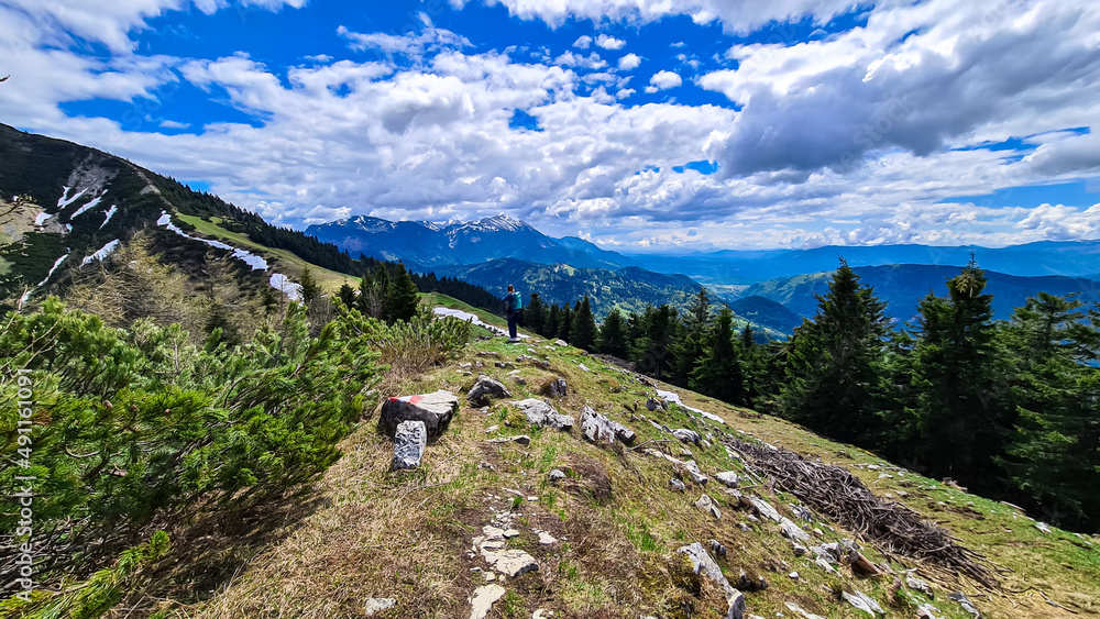 Woman hiking to the summit of Hahnkogel (Klek) with scenic view on the Karawanks, Carinthia, Austria. Borders Austria, Slovenia, Italy. Triglav National Park. Alpine meadows. Clouds coming. Awe