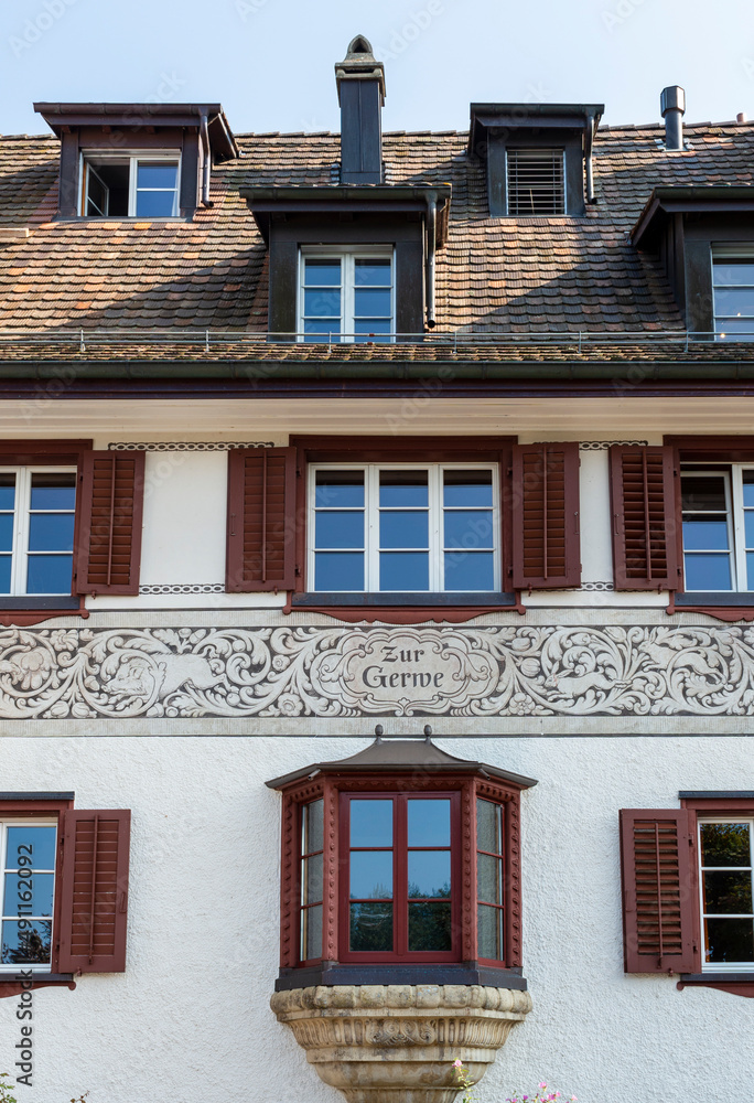 Decorative white tenement house with dark red shutters in old town in German city Würzbur, with single oriel, inscription and ornamental paintings with leaves, rabbits and wild pigs 