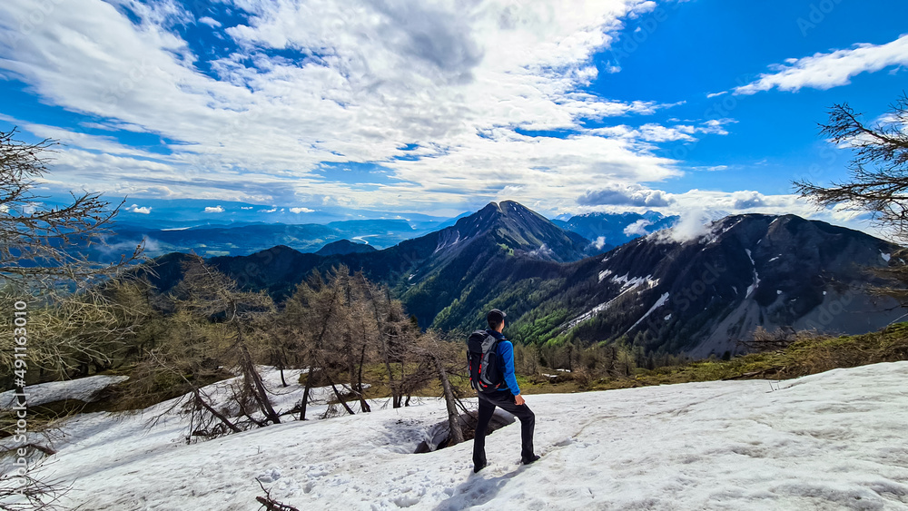 Man standing on a snow field in spring. Scenic view near Frauenkogel on mountain peaks in the Karawanks, Carinthia, Austria. Border with Slovenia. Triglav National Park. Looking on Kahlkogel (Golica).
