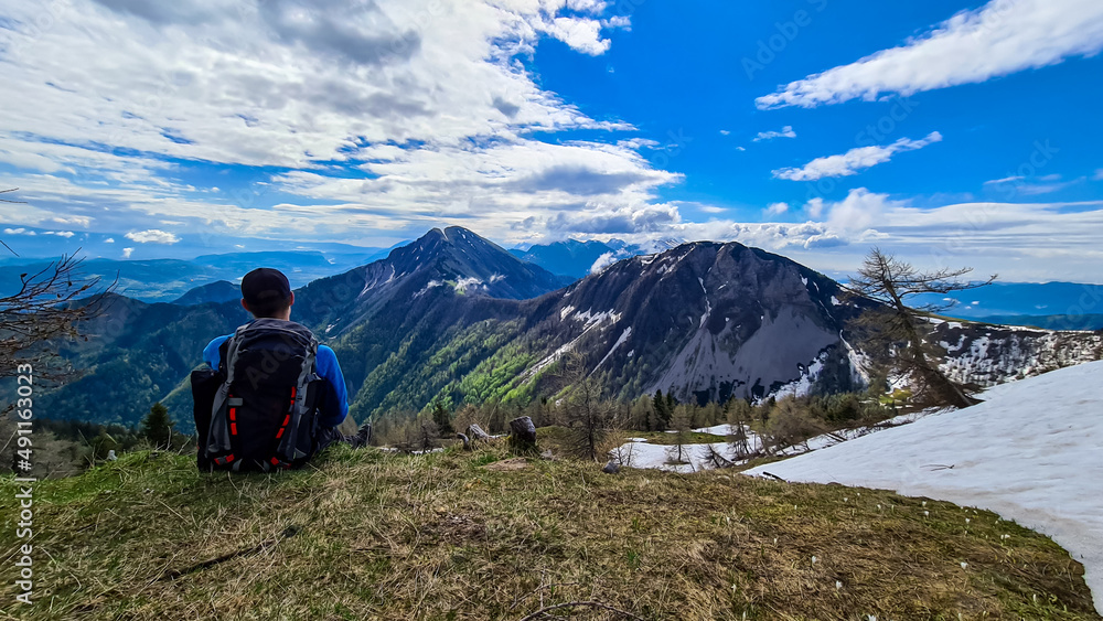 Male hiker having a break in spring on the summit of Frauenkogel in the Karawanks in Carinthia, Austria, Europe. Borders with Slovenia. Triglav National Park. Looking on Kahlkogel and Hahnkogel. Male hiker having a break in spring on the summit of Frauenkogel in the Karawanks in Carinthia, Austria, Europe. Borders with Slovenia. Triglav National Park. Looking on Kahlkogel and Hahnkogel.
