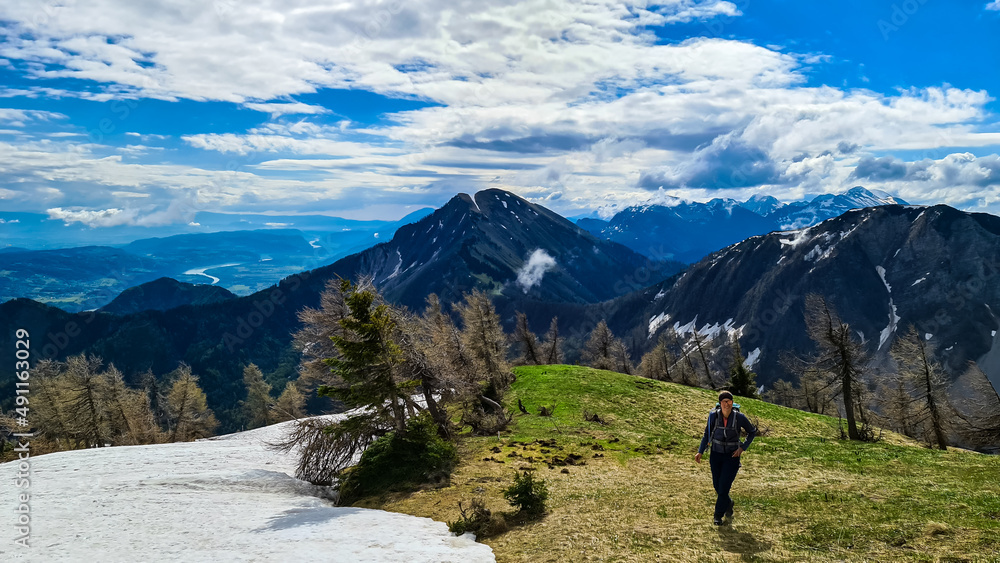 Active woman hiking on Frauenkogel with scenic view on mountain peaks in the Karawanks, Carinthia, Austria. Border with Slovenia. Triglav National Park. Kahlkogel (Golica).Snow field melting in spring