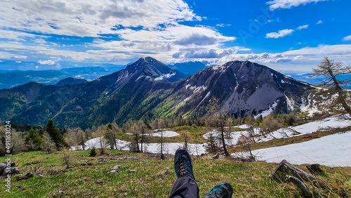 Hiker having a break in spring on the summit of Frauenkogel in the Karawanks in Carinthia, Austria, Europe. Borders with Slovenia. Triglav National Park. Looking on Kahlkogel and Hahnkogel. Boots photo