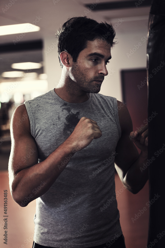 Fototapeta premium Taking it out on his punching bag. Profile of a handsome man wearing sport clothing and standing ready to punch a punching bag at the gym.