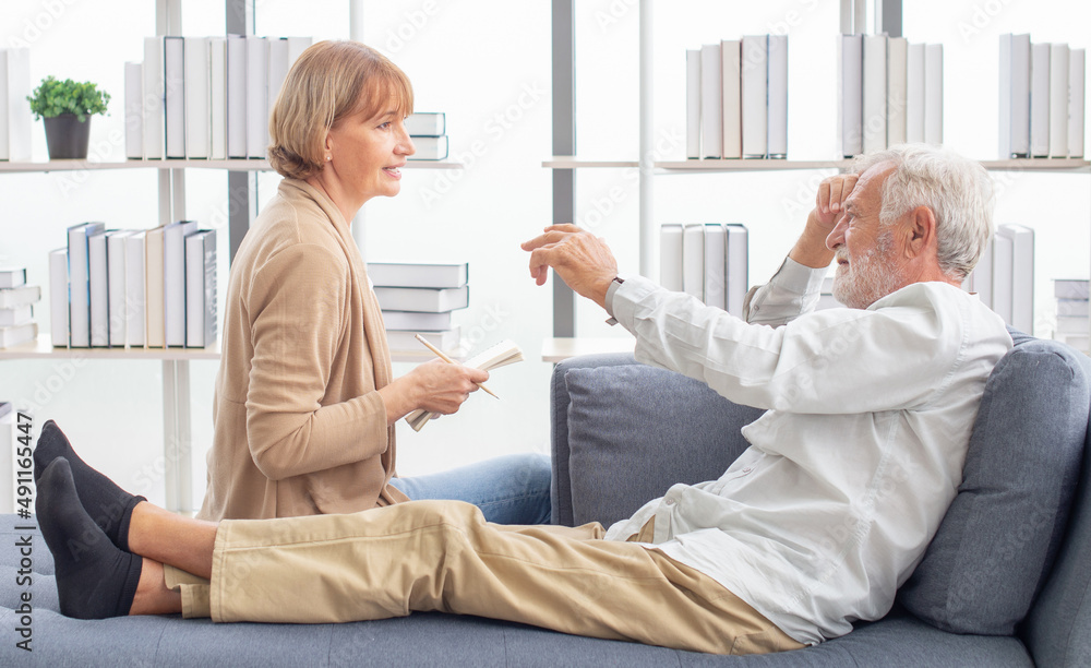 Obraz premium Senior woman supporting her ill husband lying in a sofa. Retired senior elderly husband illness with serious wife take care at home. Medical emrgency treatment and health care insurance protection 
