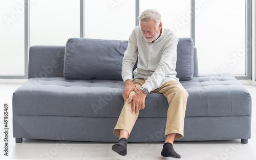 Health care and problem concept Uhappy senior man suffering from knee ache at home. Knee joint injury. Gout. Rheumatoid. Arthritis. Osteoporosis
 photo