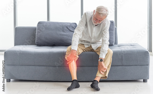 Health care and problem concept Uhappy senior man suffering from knee ache at home. Knee joint injury. Gout. Rheumatoid. Arthritis. Osteoporosis
