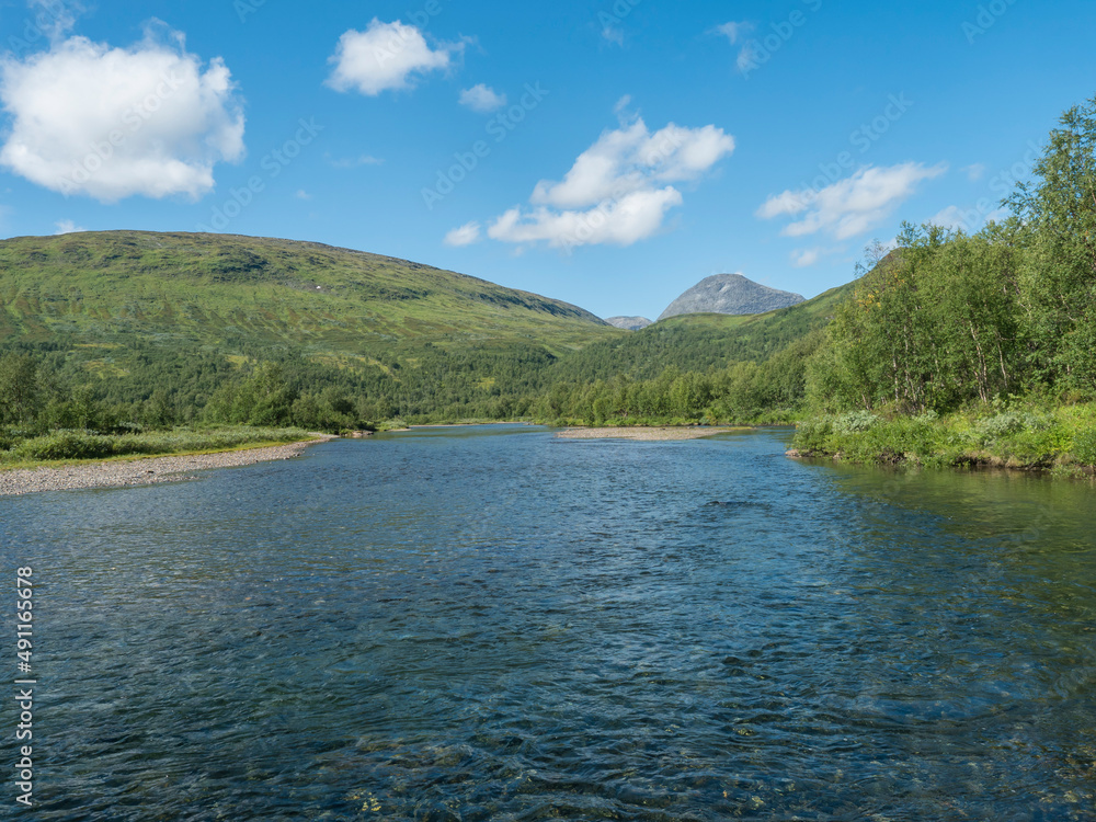 View over turquoise blue water of wild Tarra river. Tarrajakka with grassy green hills and birch tree forest along Padjelantaleden hiking trail. Summer sunny day, blue sky Lapland, Sweden