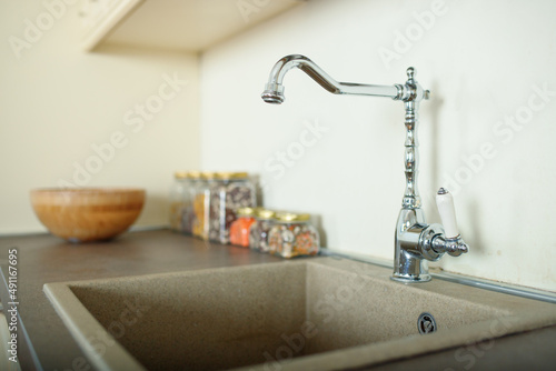 Rectangular stone kitchen sink with tall faucet in a spacious bright kitchen. Selective soft focus