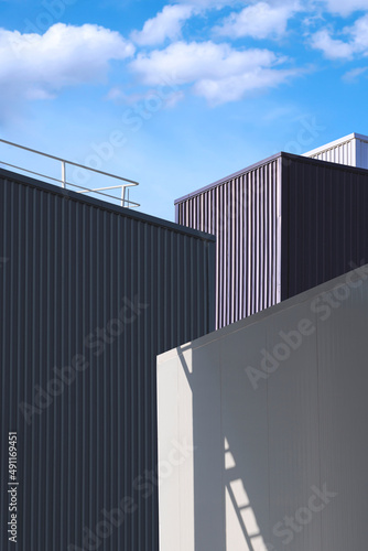 Light and shadow on surface of cold storage room with corrugated metal industrial buildings against clouds on blue sky in perspective view and vertical frame 