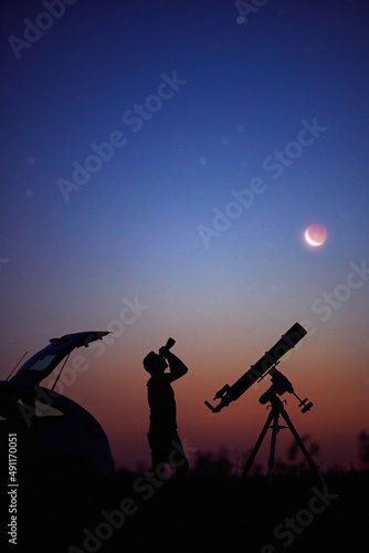 Silhouette of a man, car, telescope and countryside under the starry skies.