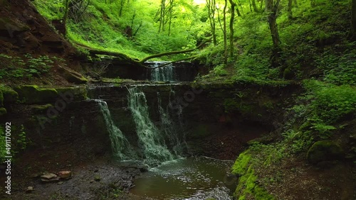 A quadcopter flies in a wooded green canyon over an exotic waterfall. Filmed in UHD 4k video.