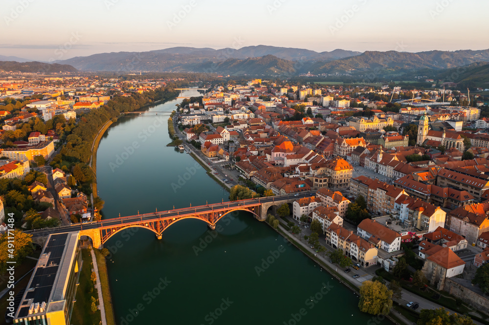 City of Maribor in Slovenia illuminated by rising sun in the summer morning. Lovely town with river flowing in the middle from aerial perspective. Touristic destination from above.
