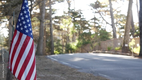 American flag, star-spangled banner by road in cypress or pine coniferous forest, scenic 17-mile drive, Monterey nature, California USA. Tourist road trip, ecotourism journey and hitchhiking traveling