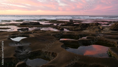 Eroded rock formation, tide pool shape in La Jolla, California coast, USA. Littoral intertidal zone erosion, tidepool relief. Sunset sky reflection in water, cavity, hollows and holes on stone surface
