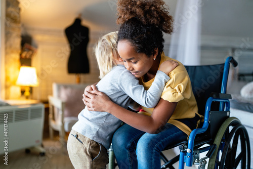 Black little girl with disability in wheelchair hugging with her younger brother.