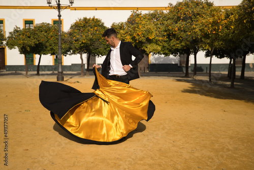 Young Spanish man in black shirt, jacket and pants, with dancing shoes, dancing flamenco with black and gold capote in the street. Typical Spanish concept, art, dance, culture, tradition.