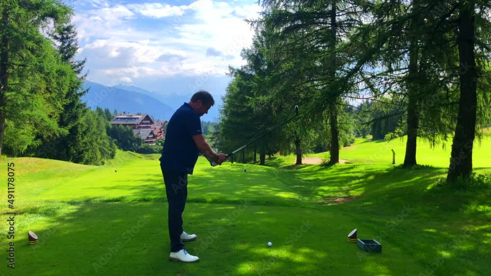 Golfer Teeing Off with Success His 3 Wood on Golf Course with Mountain View in a Sunny Summer Day in Crans Montana, Valais in Switzerland. Golfer Teeing Off with Success His 3 Wood on Golf Course with Mountain View in a Sunny Summer Day in Crans Montana, Valais in Switzerland.