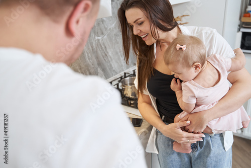 Young Caucasian female with kid is looking ahead while standing in room indoors
