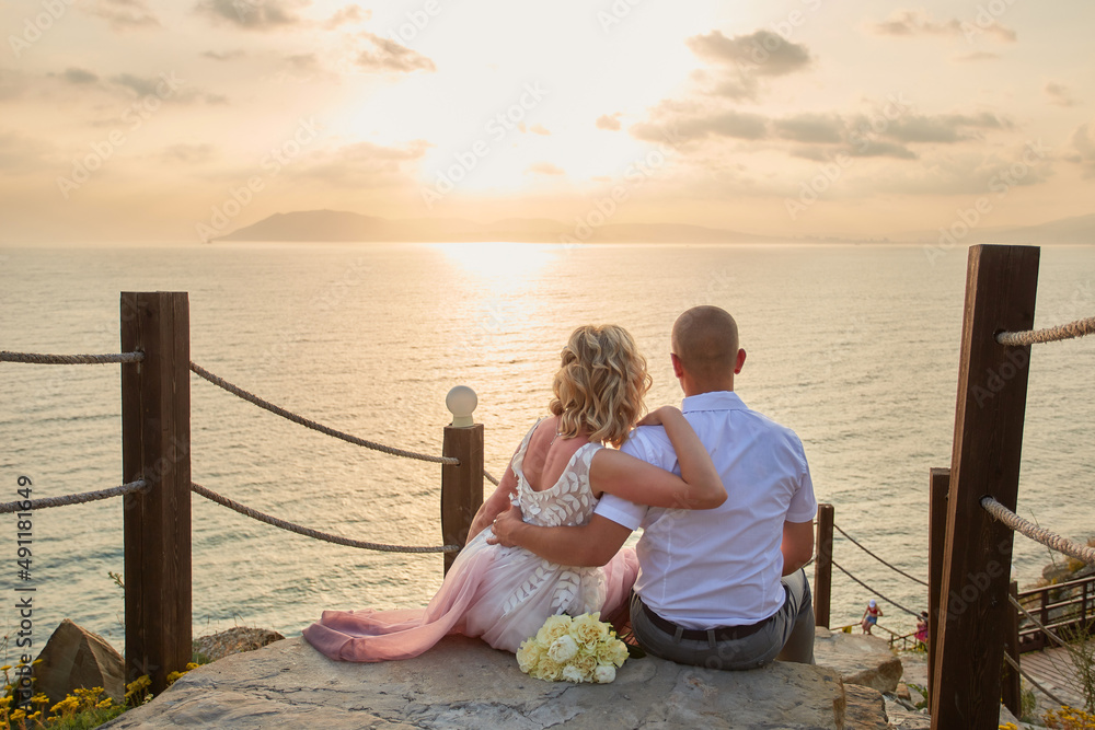 Just married couple admires a beautiful sunset on the sea. View from the back