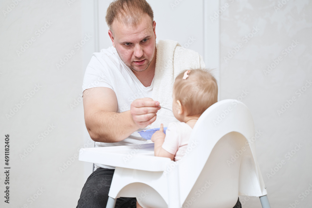 Dad with stubble in white clothes spending time with his daughter during the breakfast at home Dad with stubble in white clothes spending time with his daughter during the breakfast at home
