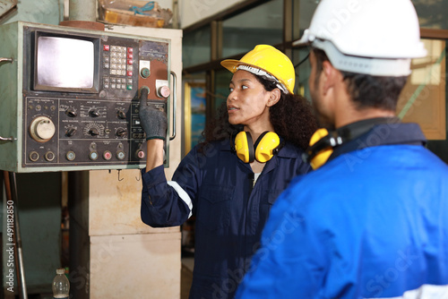 Technician engineer woman in protective uniform with hardhat standing and teaching apprentices or colleague worker to use computerized machine control at heavy industry manufacturing factory