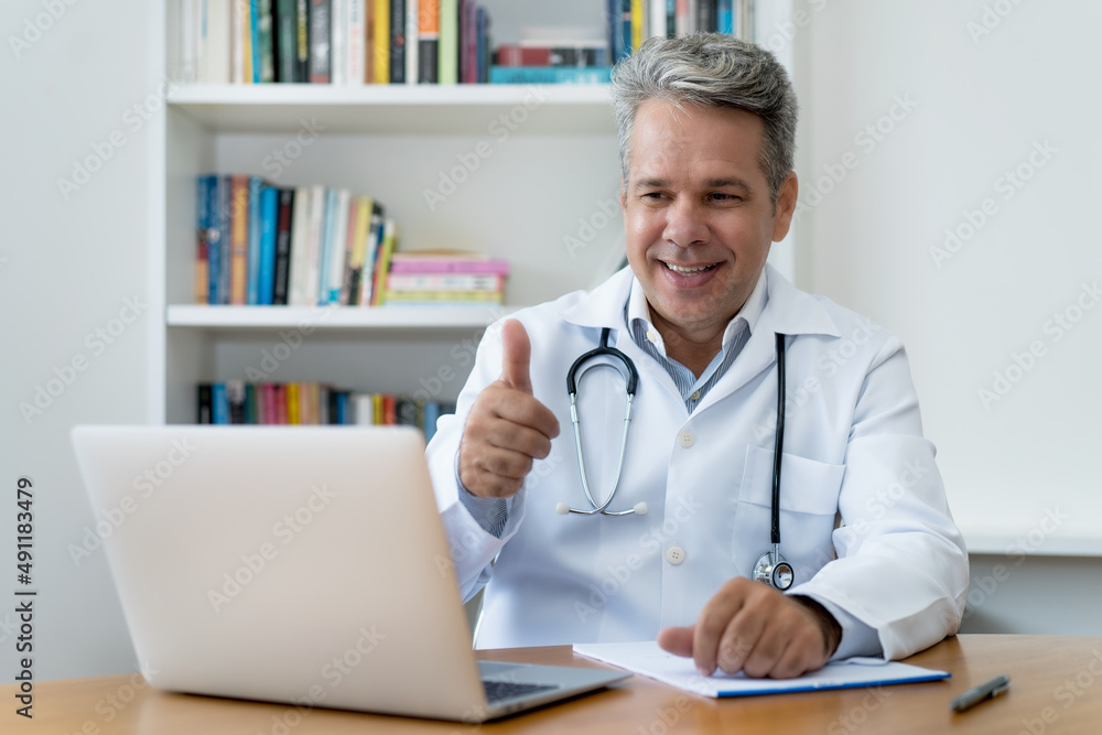 Laughing senior doctor with gray hair with good news for patient at video call Laughing senior doctor with gray hair with good news for patient at video call