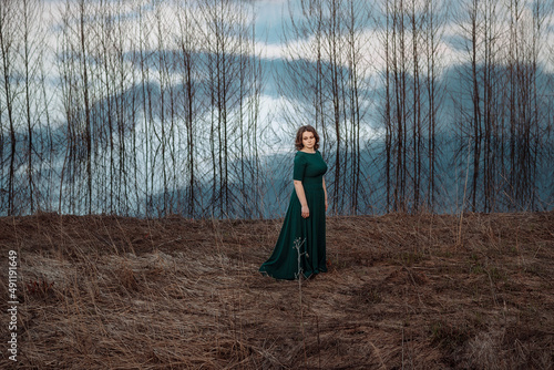 Foto Woman in a long dress stands by the water, river, lake, which reflects bare tree