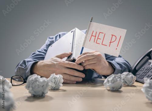 Frustrated and overworked businessman burying his head under a laptop computer asking for help photo