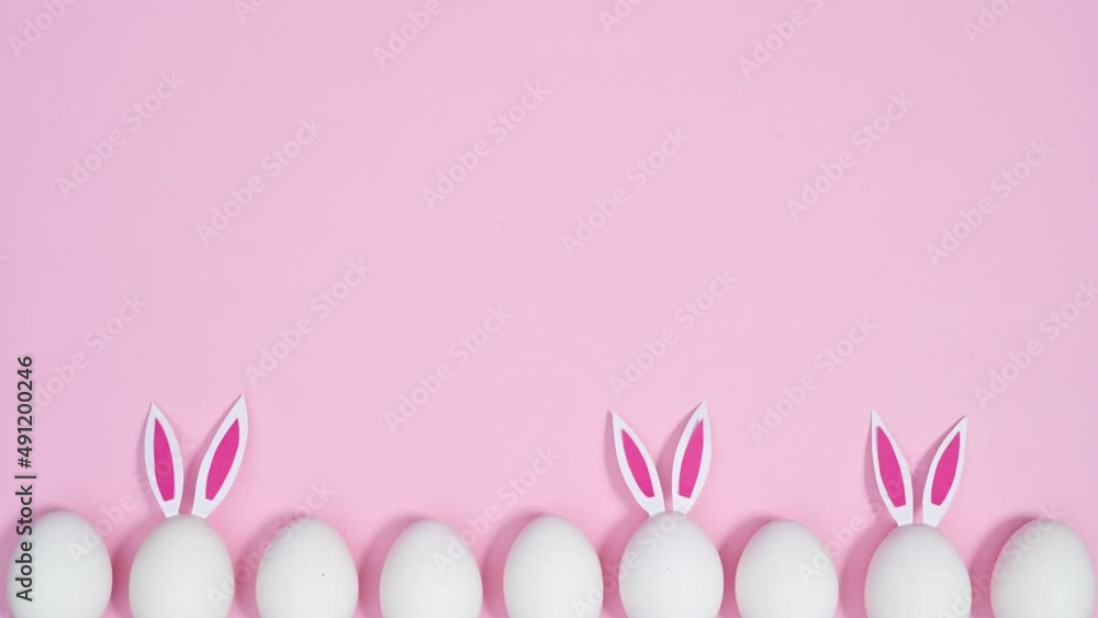 White Easter eggs with rabbit ears appear on pastel pink background. Flat lay stop motion copy space White Easter eggs with rabbit ears appear on pastel pink background. Flat lay stop motion copy space