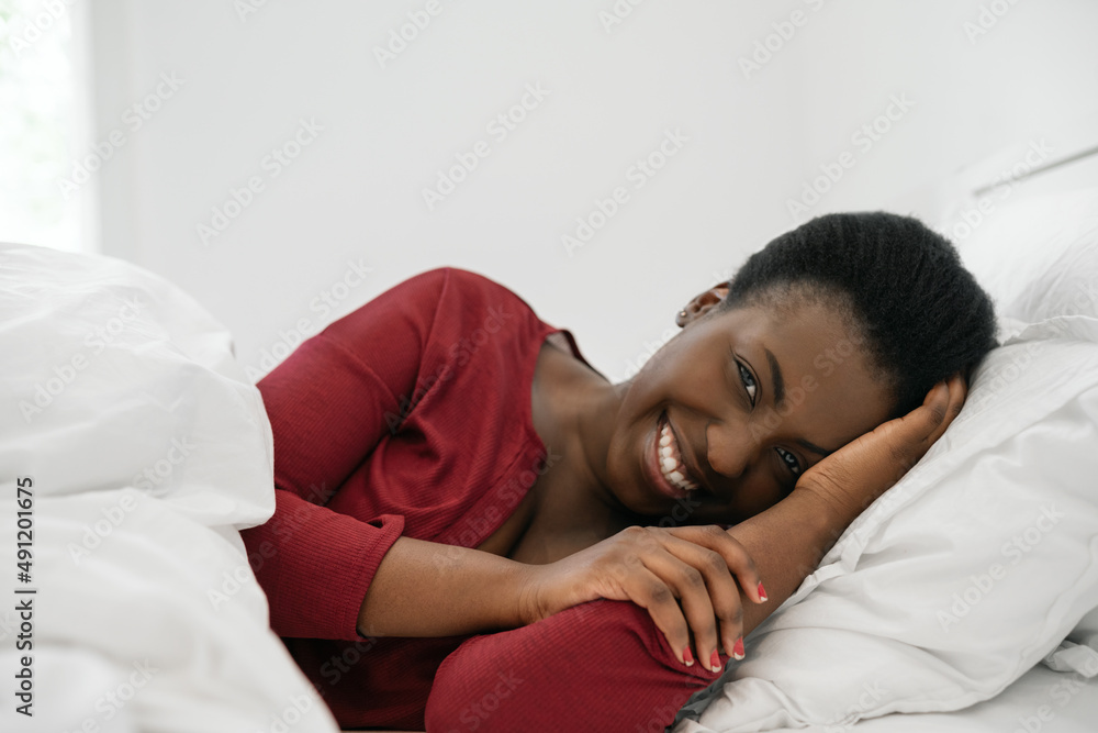 Black African woman laying in bed, smiling and looking at camera Black African woman laying in bed, smiling and looking at camera