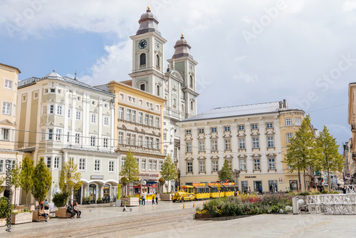 Linz, Austria, 27 August 2021: Baroque Old Cathedral or Alter Dom with two towers, Church of Ignatius, Hauptplatz or main square at sunny summer day, Facade of stone colorful historical buildings photo