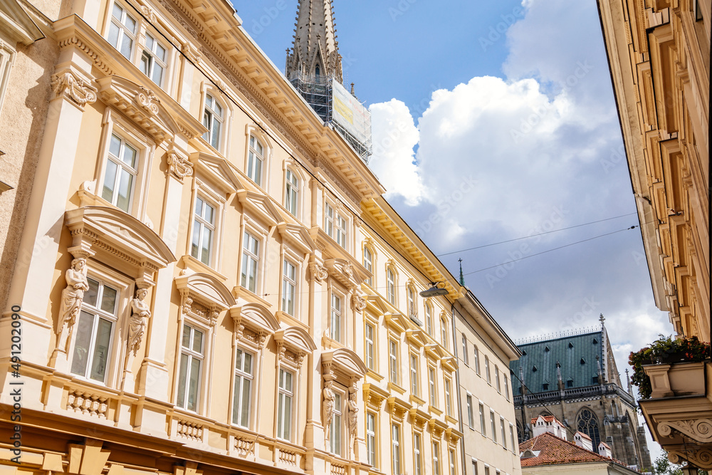 Fototapeta premium Linz, Austria, 27 August 2021: Narrow picturesque street, Facade of colorful buildings in historic center of medieval city, renaissance and baroque houses at summer sunny day, cafe with wooden windows