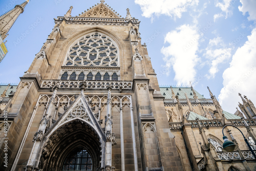 Linz, Austria, 27 August 2021: Facade of medieval catholic stone gothic New Cathedral of Immaculate Conception with arch, old town street at sunny summer day, lancet windows and carved statues