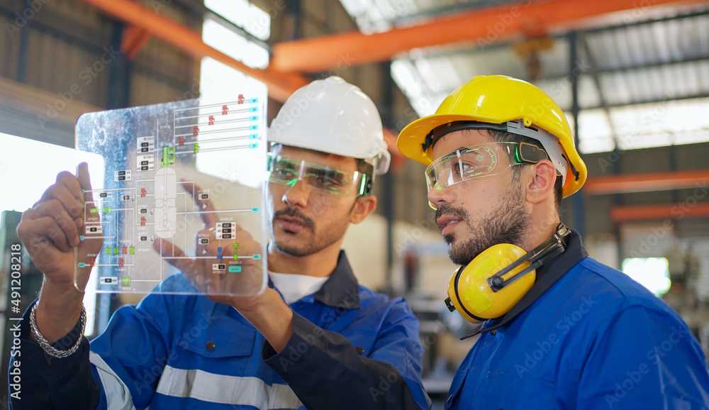 Engineer wearing safety helmet and glasses and explain the project diagram with manager in the manufacturing factory. Worker holding transparent futuristic tablet. Industrial, technology concept. Engineer wearing safety helmet and glasses and explain the project diagram with manager in the manufacturing factory. Worker holding transparent futuristic tablet. Industrial, technology concept.