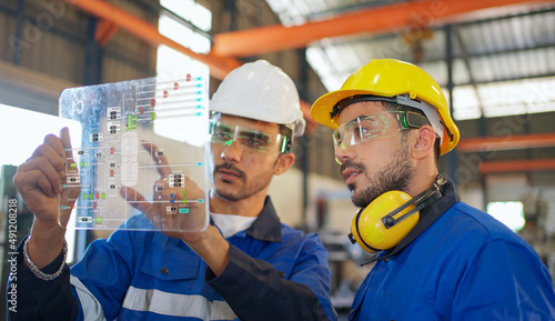 Engineer wearing safety helmet and glasses and explain the project diagram with manager in the manufacturing factory. Worker holding transparent futuristic tablet. Industrial, technology concept.