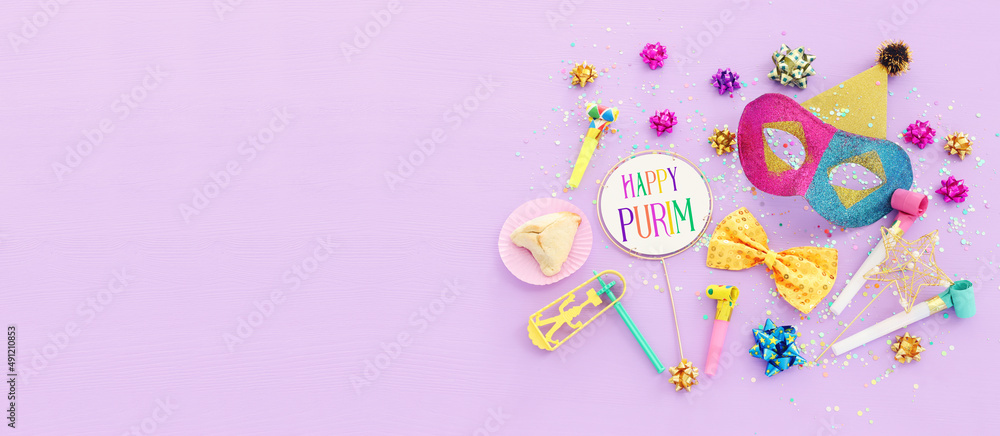 Purim celebration concept (jewish carnival holiday) over purple wooden background