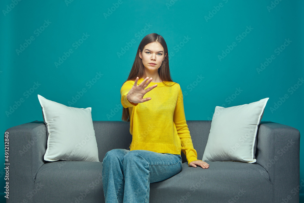 Serious girl show stop gesture, protest against gender discrimination, domestic violence, sitting on sofa. Woman rights Serious girl show stop gesture, protest against gender discrimination, domestic violence, sitting on sofa. Woman rights